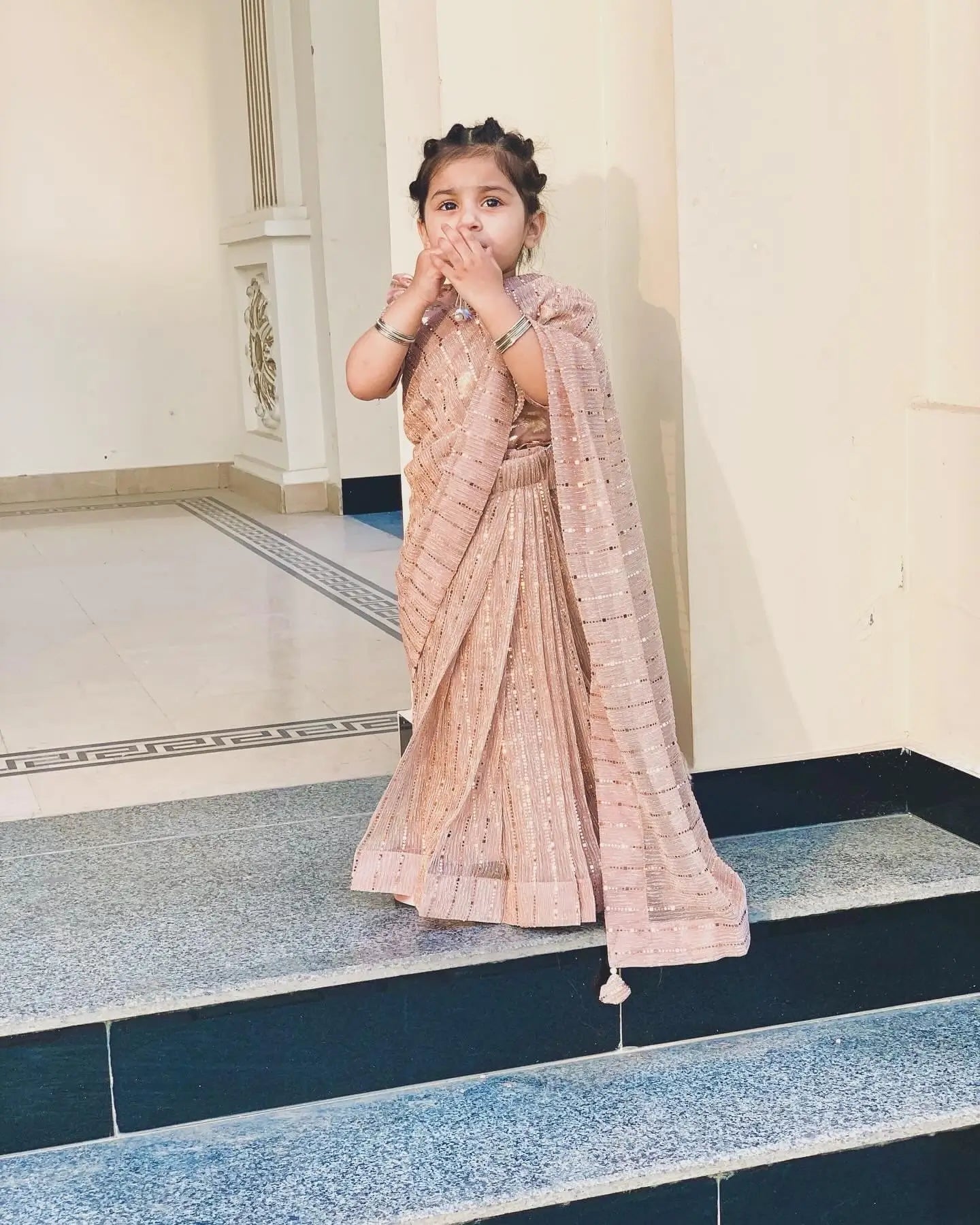 Child in a traditional saree standing on a tiled floor.