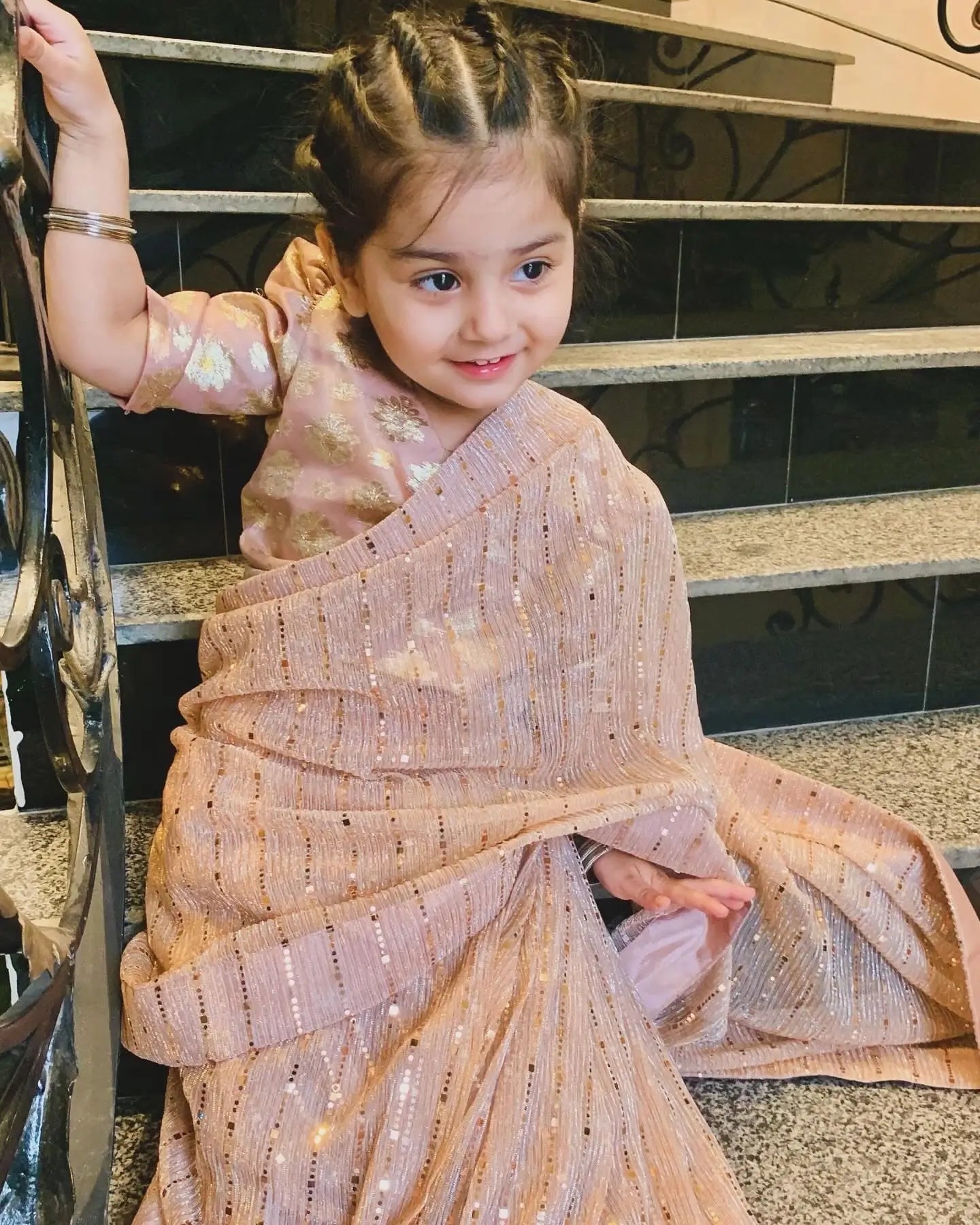Child wearing a traditional outfit with a decorative pattern, standing on a staircase.
